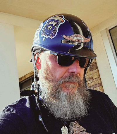 A bearded biker wearing a black polo-style reversible beanie helmet with a Harley logo, sunglasses, and a black shirt.